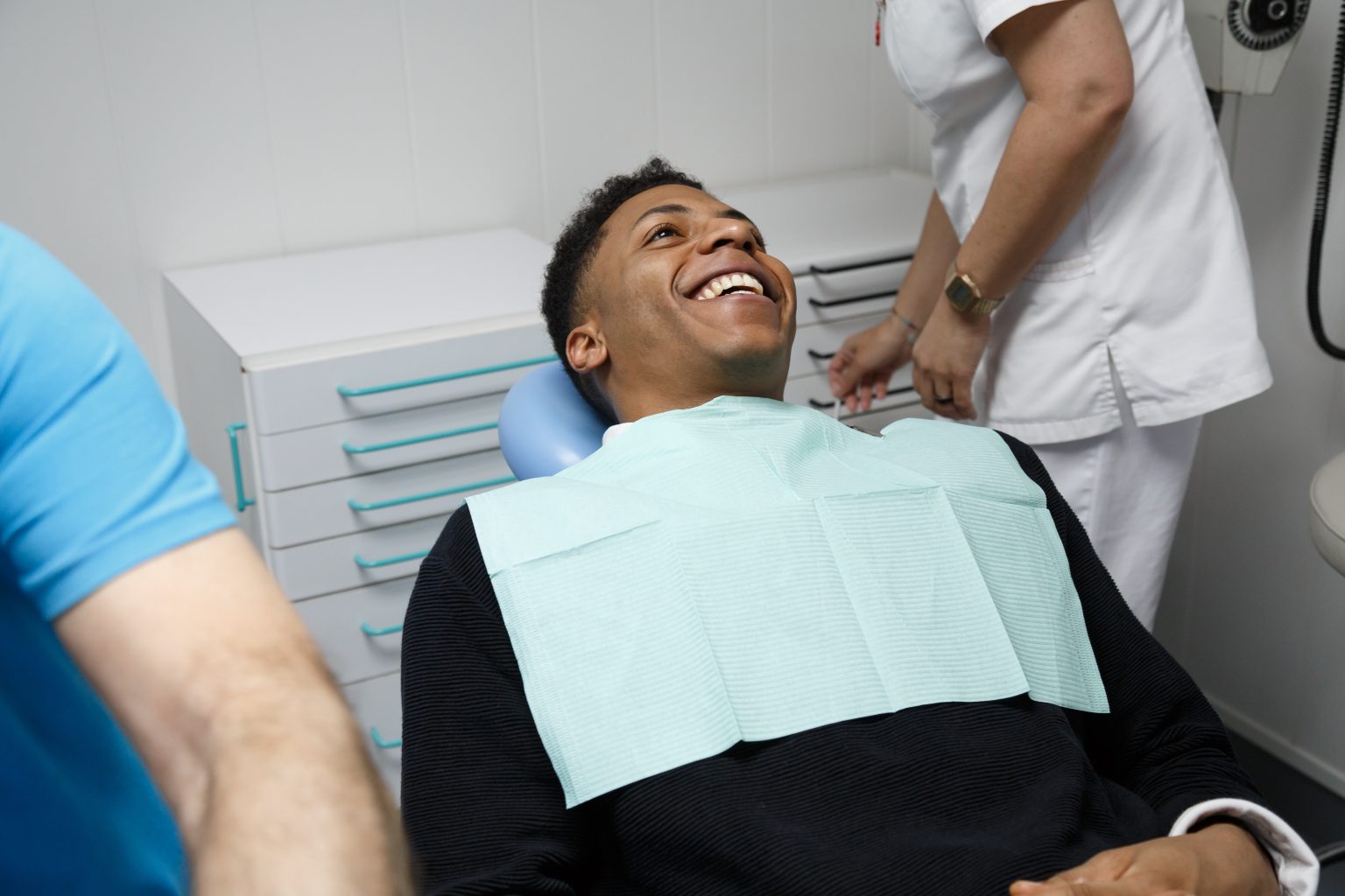 Laughing African American Man Sitting In Chair Of Dentist In Clinic And Preparing For Procedure With Nurse.